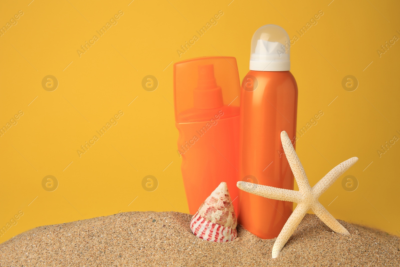 Photo of Sand with bottles of sunscreens, starfish and seashell against orange background, space for text. Sun protection