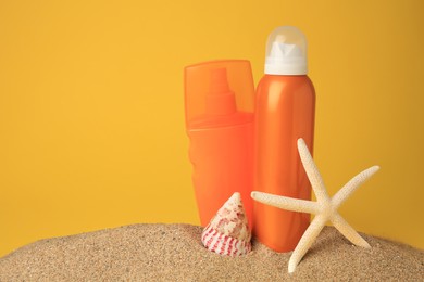 Photo of Sand with bottles of sunscreens, starfish and seashell against orange background, space for text. Sun protection