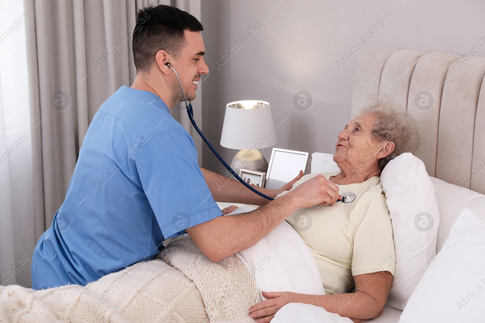 Photo of Young caregiver examining senior woman in bedroom. Home health care service