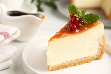 Photo of Piece of delicious caramel cheesecake with red currants and mint served on white table, closeup