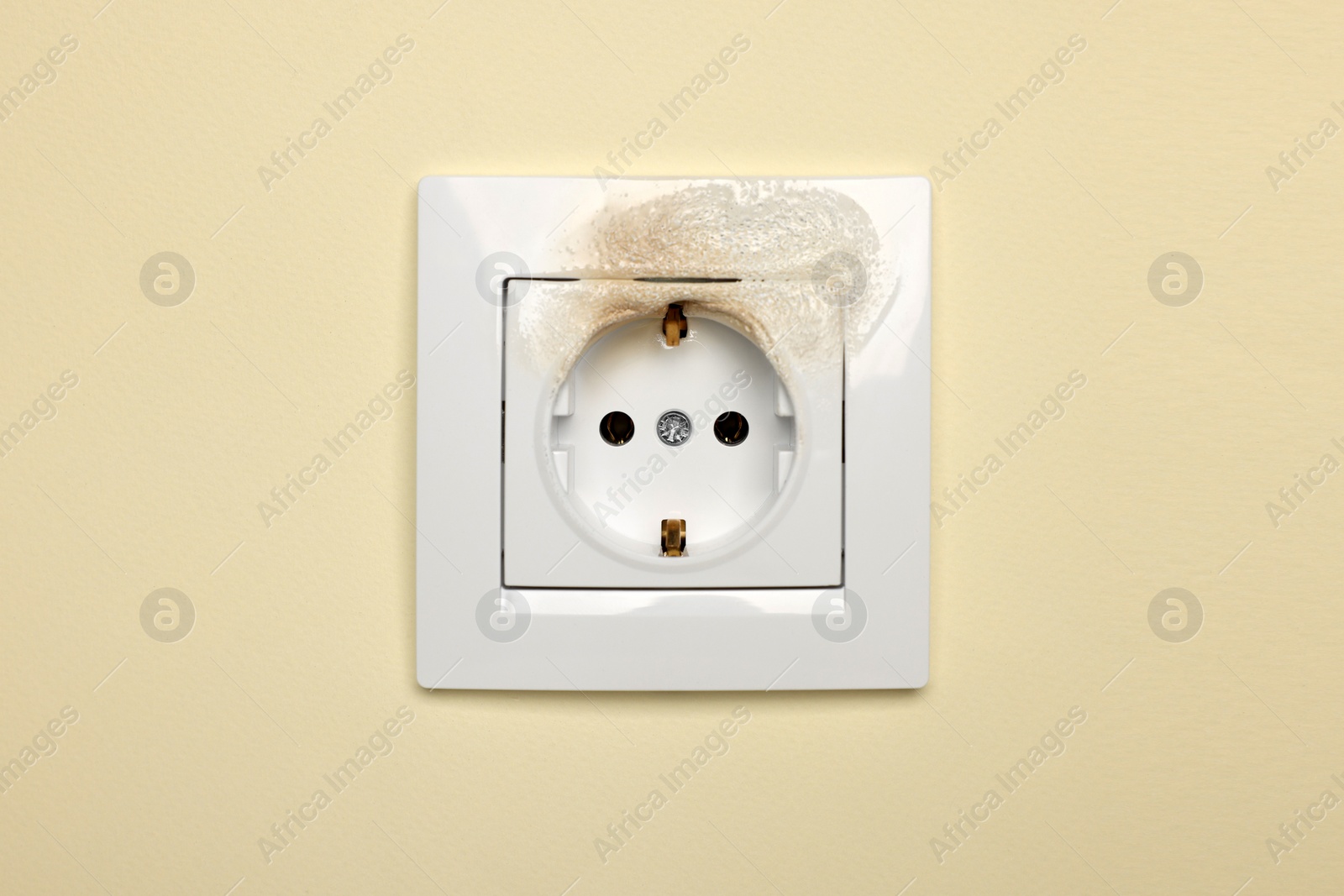 Photo of Burnt power socket on beige wall. Electrical short circuit