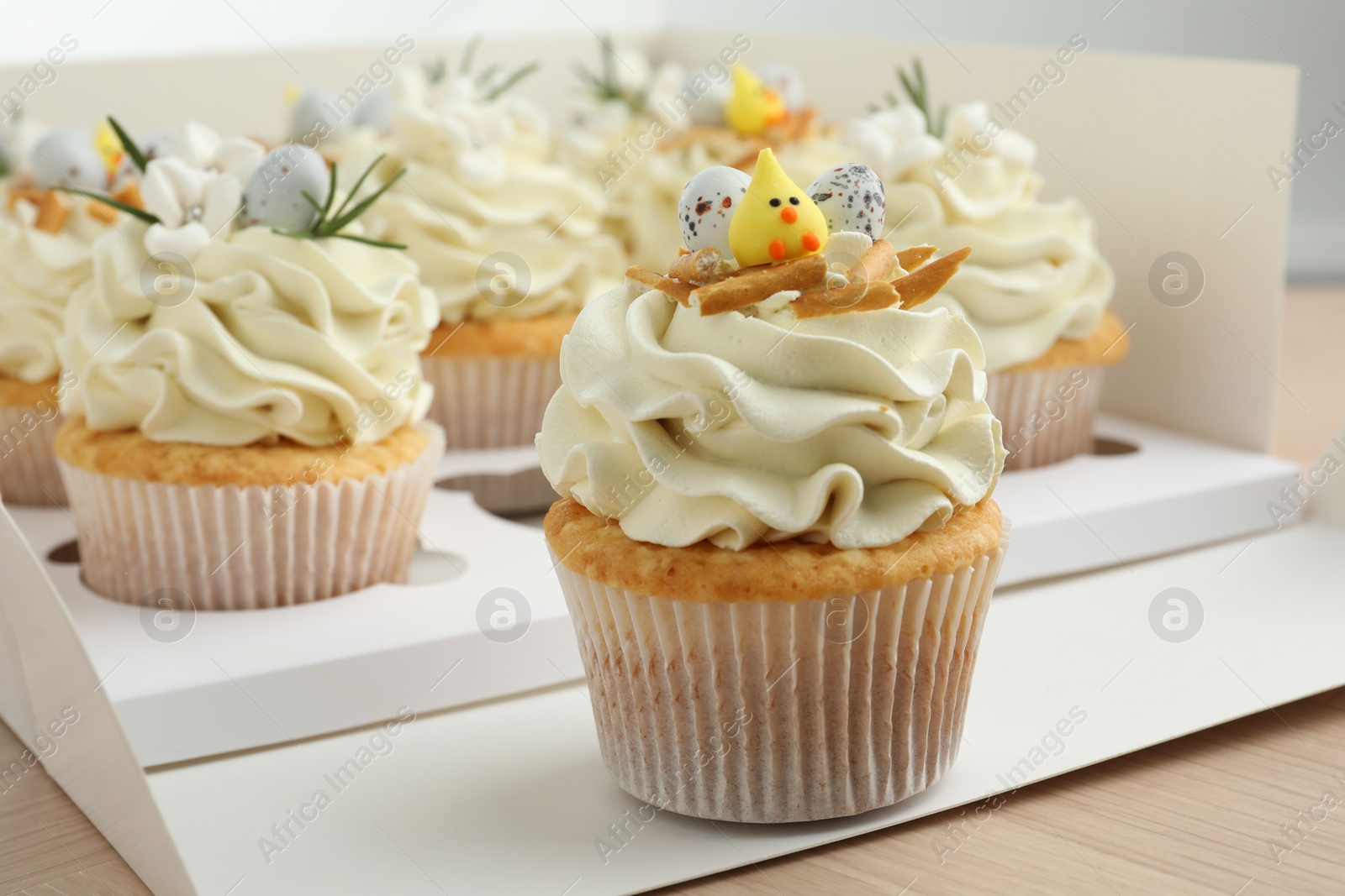 Photo of Tasty Easter cupcakes in box on wooden table, closeup