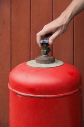 Photo of Man opening red gas cylinder near brown wooden wall, closeup