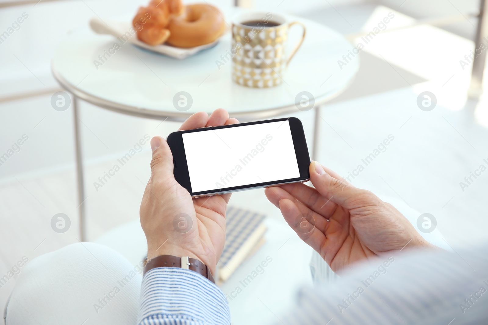 Photo of Young man holding mobile phone with blank screen in hands, indoors