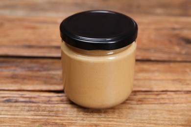 Photo of Tasty nut paste in jar on wooden table, closeup