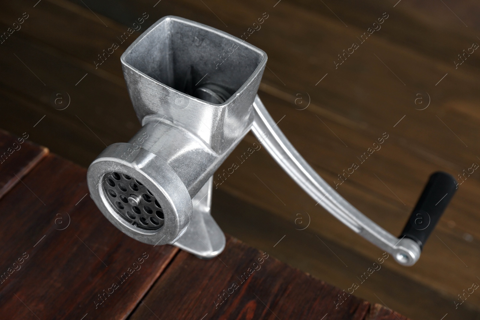 Photo of Metal manual meat grinder on wooden table, closeup