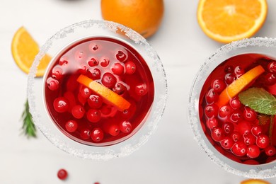 Tasty cranberry cocktail with rosemary and oranges in glasses on white table, flat lay