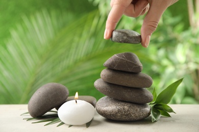 Photo of Woman stacking stones on table against blurred background, closeup. Zen concept
