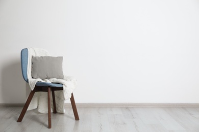 Photo of Stylish chair with pillow and plaid near white wall. Idea for interior design