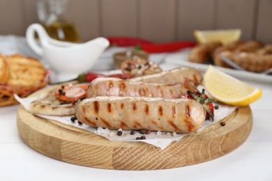 Tasty grilled sausages with vegetables, lemon and spices on white wooden table, closeup