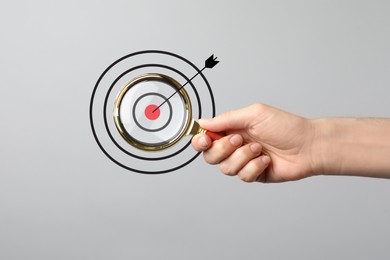 Image of Woman holding magnifying glass on light grey background, closeup. Illustration of target and arrow