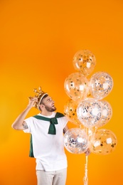 Photo of Young man with crown and air balloons on color background