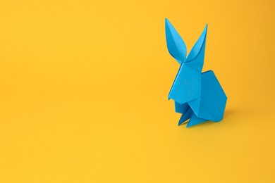 Photo of Origami art. Handmade light blue paper bunny on yellow background, space for text