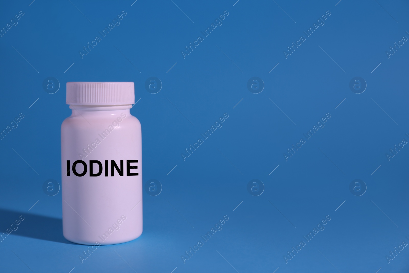 Photo of Plastic container of medical iodine on light blue background, space for text