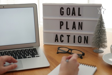 Photo of Woman working at wooden table, closeup. Light box with words Goal Plan Action on workplace