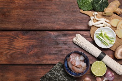 Photo of Cooking delicious ramen soup. Different ingredients on wooden table, flat lay. Space for text
