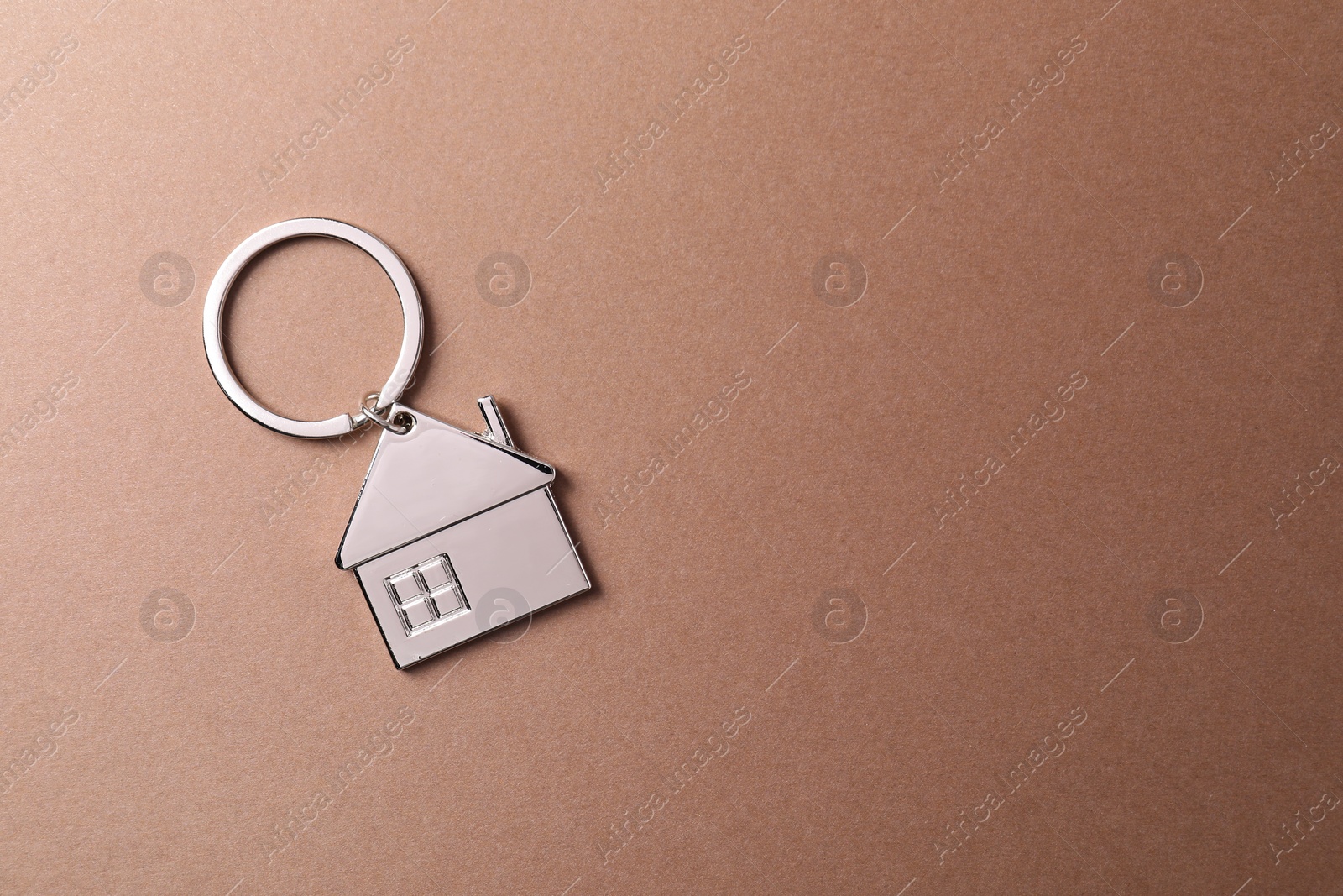 Photo of Metallic keychain in shape of house on light brown background, top view. Space for text
