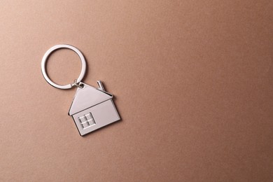 Metallic keychain in shape of house on light brown background, top view. Space for text