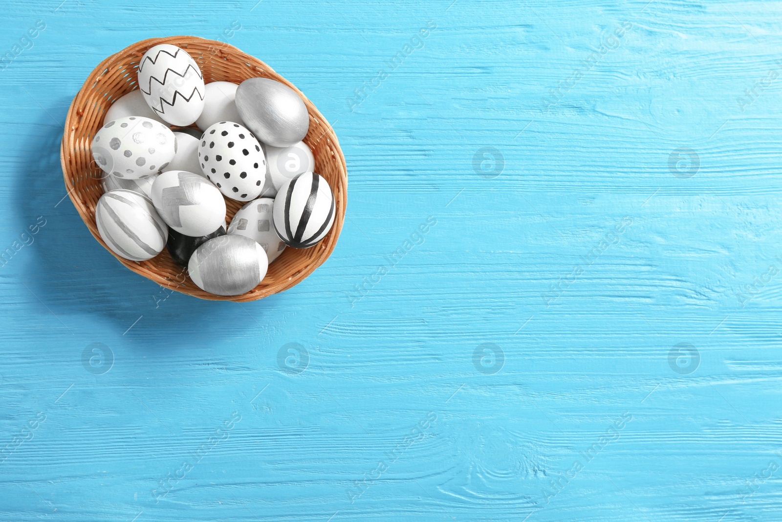 Photo of Wicker bowl of Easter eggs on wooden background, top view with space for text