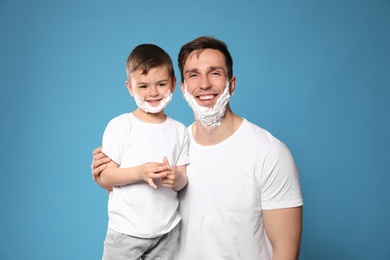 Photo of Dad and his little son with shaving foam on faces against color background
