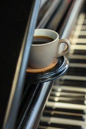 Photo of Cup of delicious coffee on grand piano, closeup