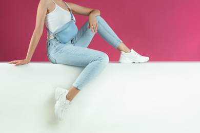 Woman in stylish sneakers sitting on color background, closeup