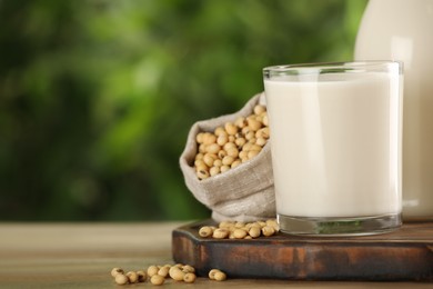 Glass with fresh soy milk and grains on white wooden table against blurred background, closeup. Space for text