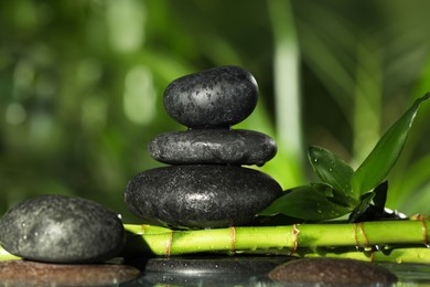 Photo of Wet stacked stones on bamboo stems against blurred background, closeup