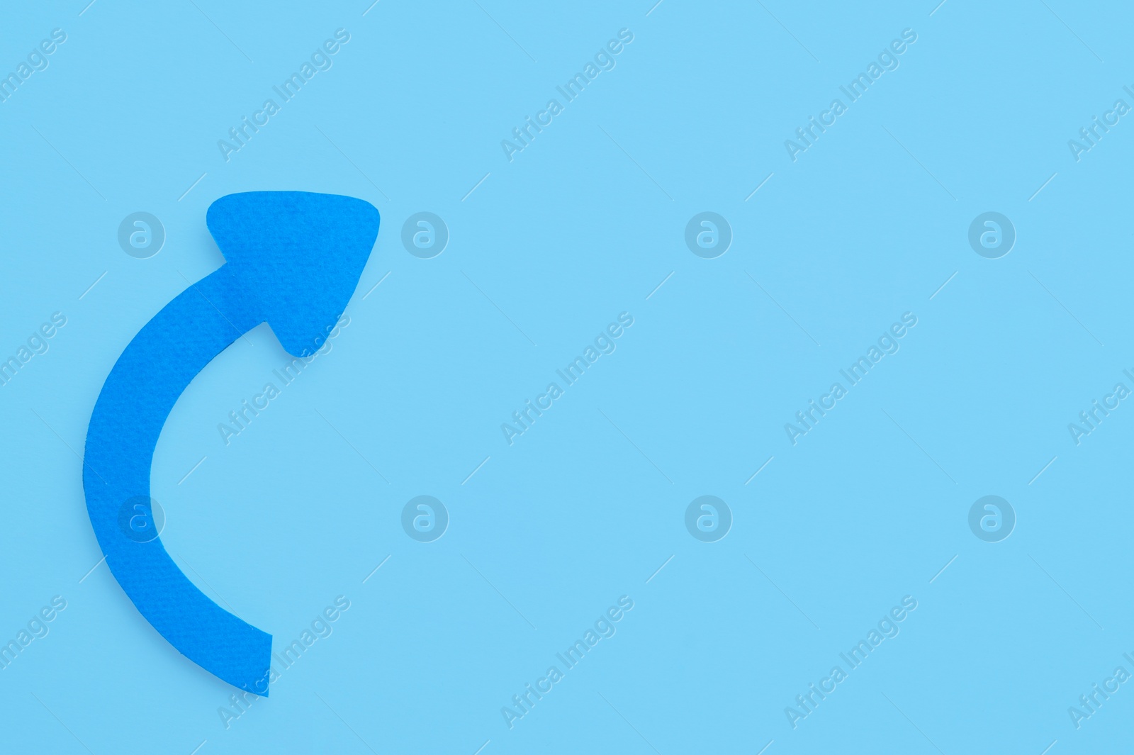 Photo of Paper curved arrow on light blue background, top view. Space for text