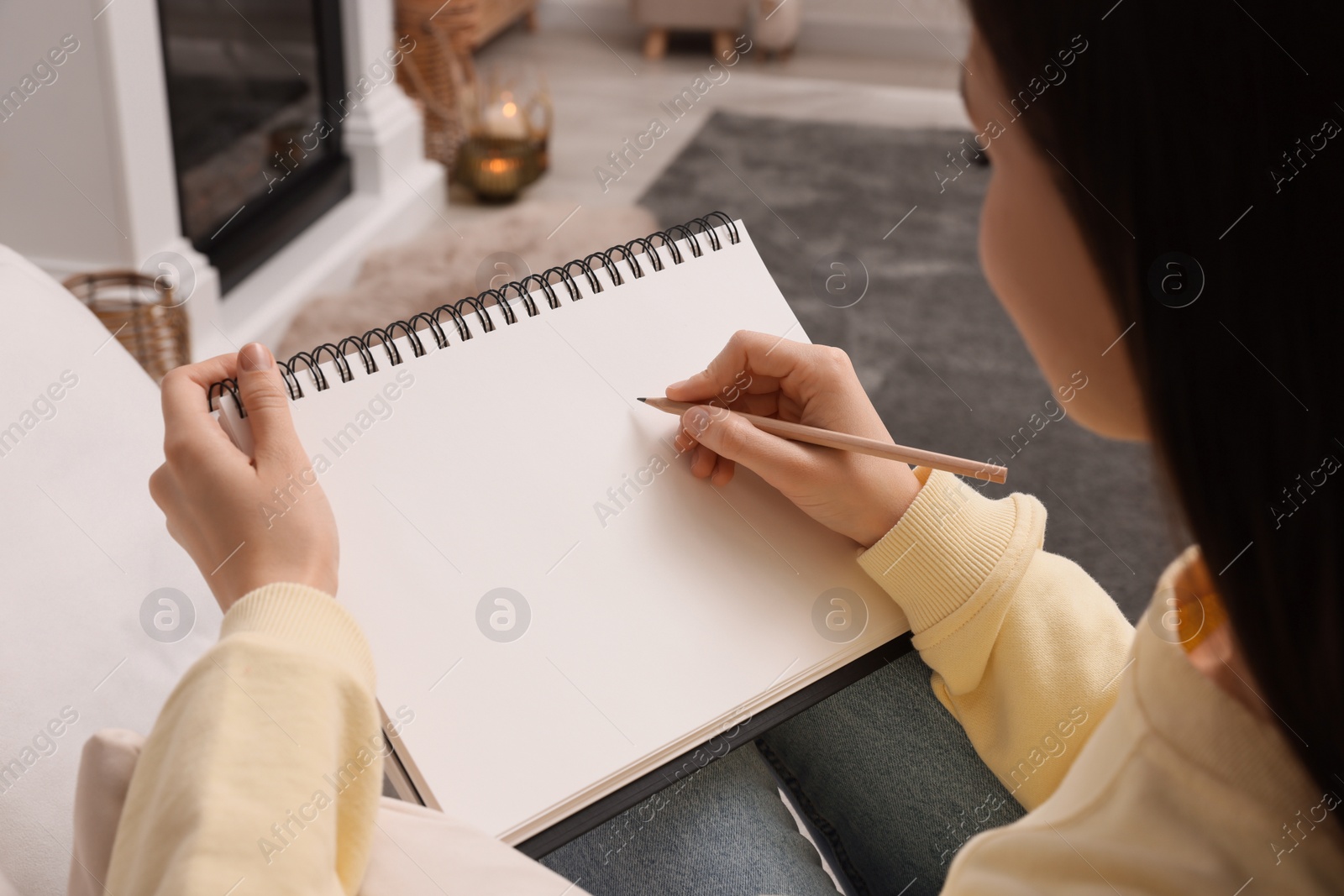 Photo of Young woman drawing in sketchbook at home, closeup