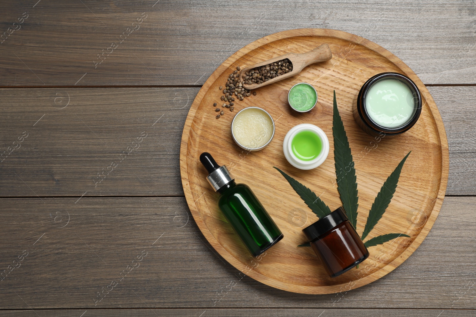 Photo of Different hemp cosmetics, green leaf and seeds on wooden table, top view. Space for text