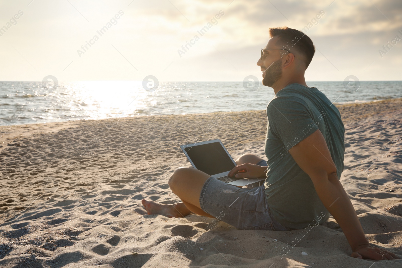 Photo of Man working with laptop on beach. Space for text