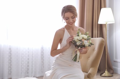 Beautiful young bride in elegant wedding dress with bouquet sitting in armchair