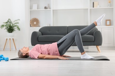 Photo of Senior woman in sportswear doing exercises on fitness mat at home