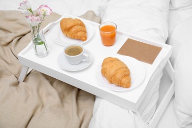 Photo of Tray with tasty croissants, drinks and flowers on bed
