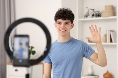 Smiling teenage blogger waving hello to his subscribers while streaming at home