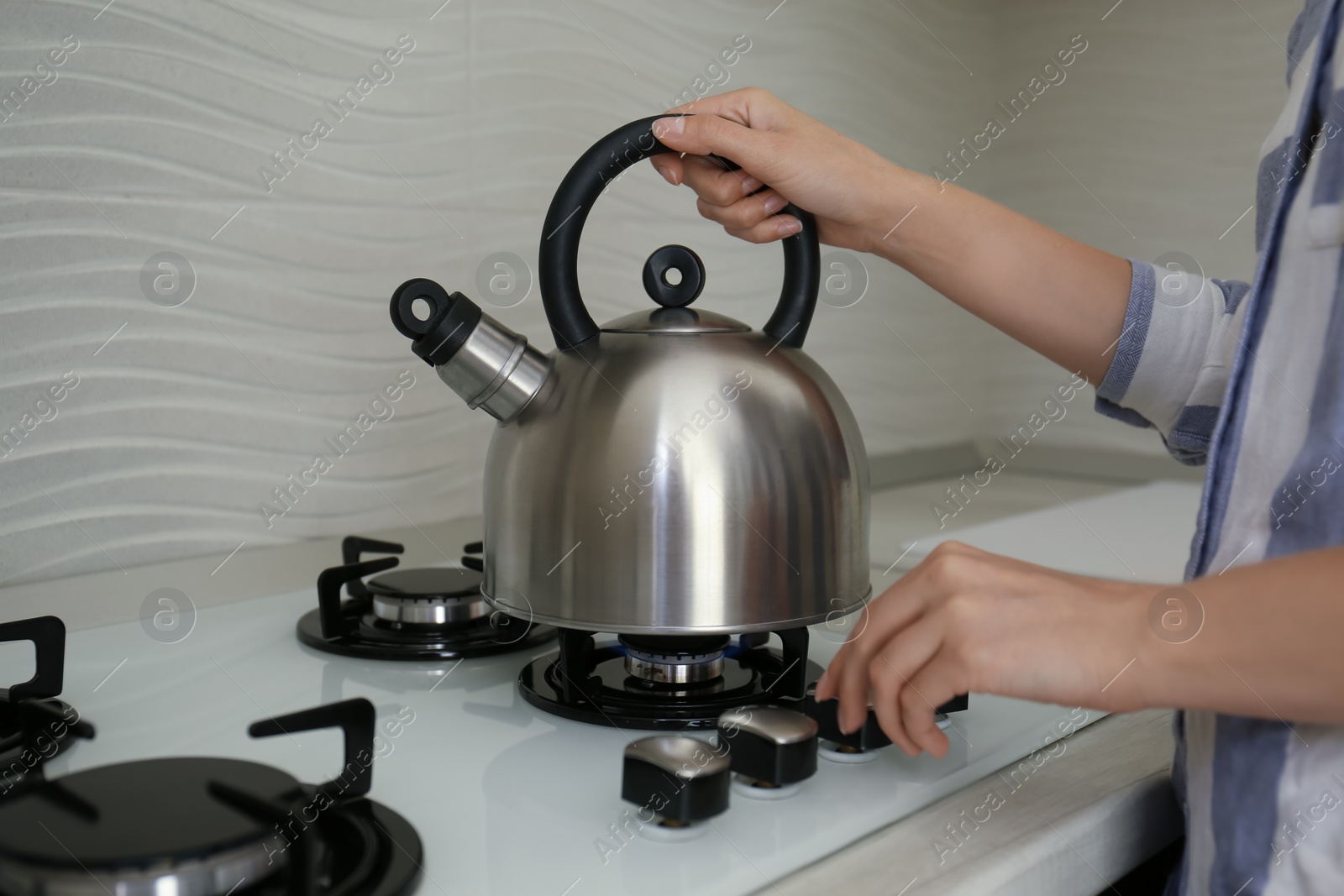 Photo of Woman putting kettle on gas stove in kitchen, closeup