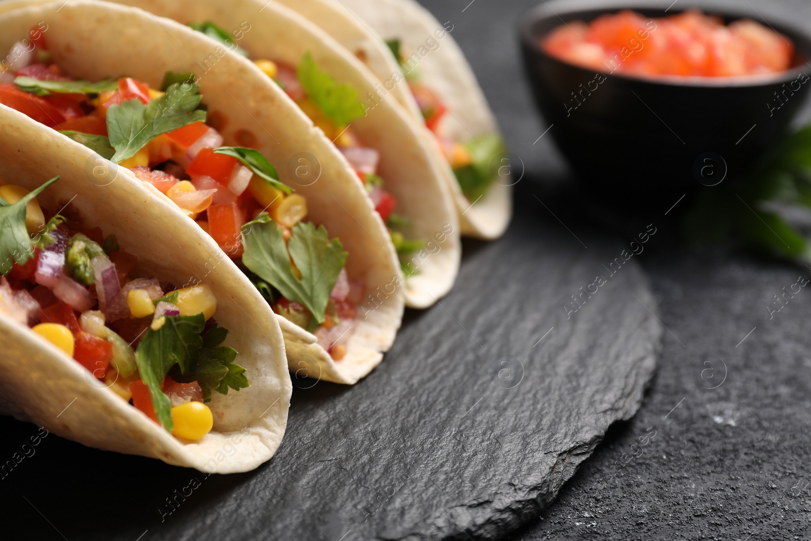 Photo of Tasty tacos with vegetables on black textured table, closeup. Space for text