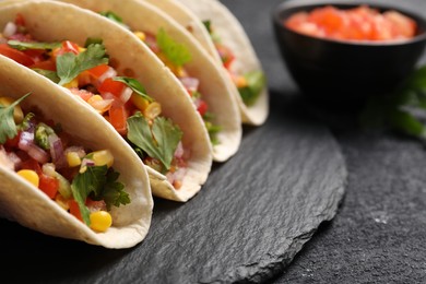 Tasty tacos with vegetables on black textured table, closeup. Space for text