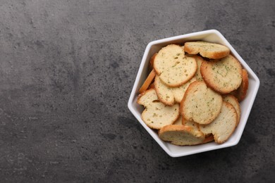 Photo of Crispy rusks in bowl on grey table, top view. Space for text