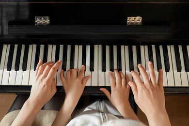 Photo of Young woman with child playing piano, above view. Music lesson