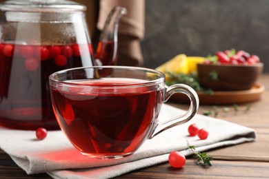 Photo of Tasty hot cranberry tea in glass cup and fresh berries on wooden table