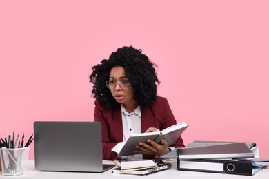 Photo of Stressful deadline. Tired woman working at white desk against pink background