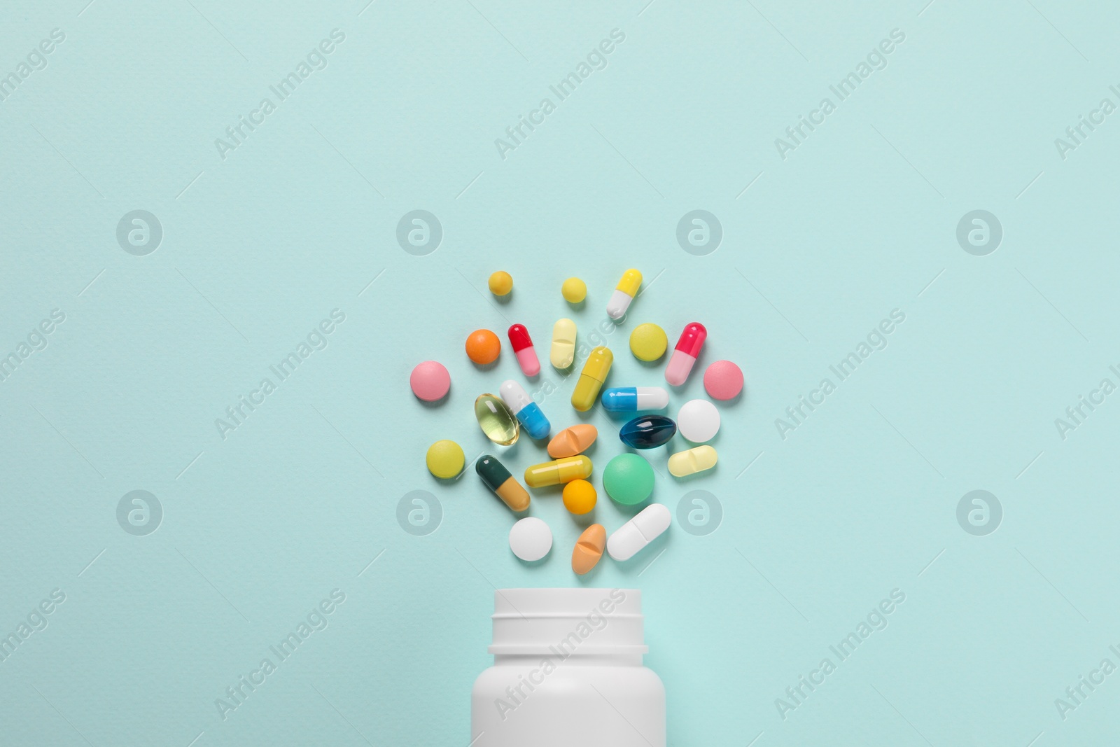 Photo of Plastic bottle with many different pills on light blue background, flat lay