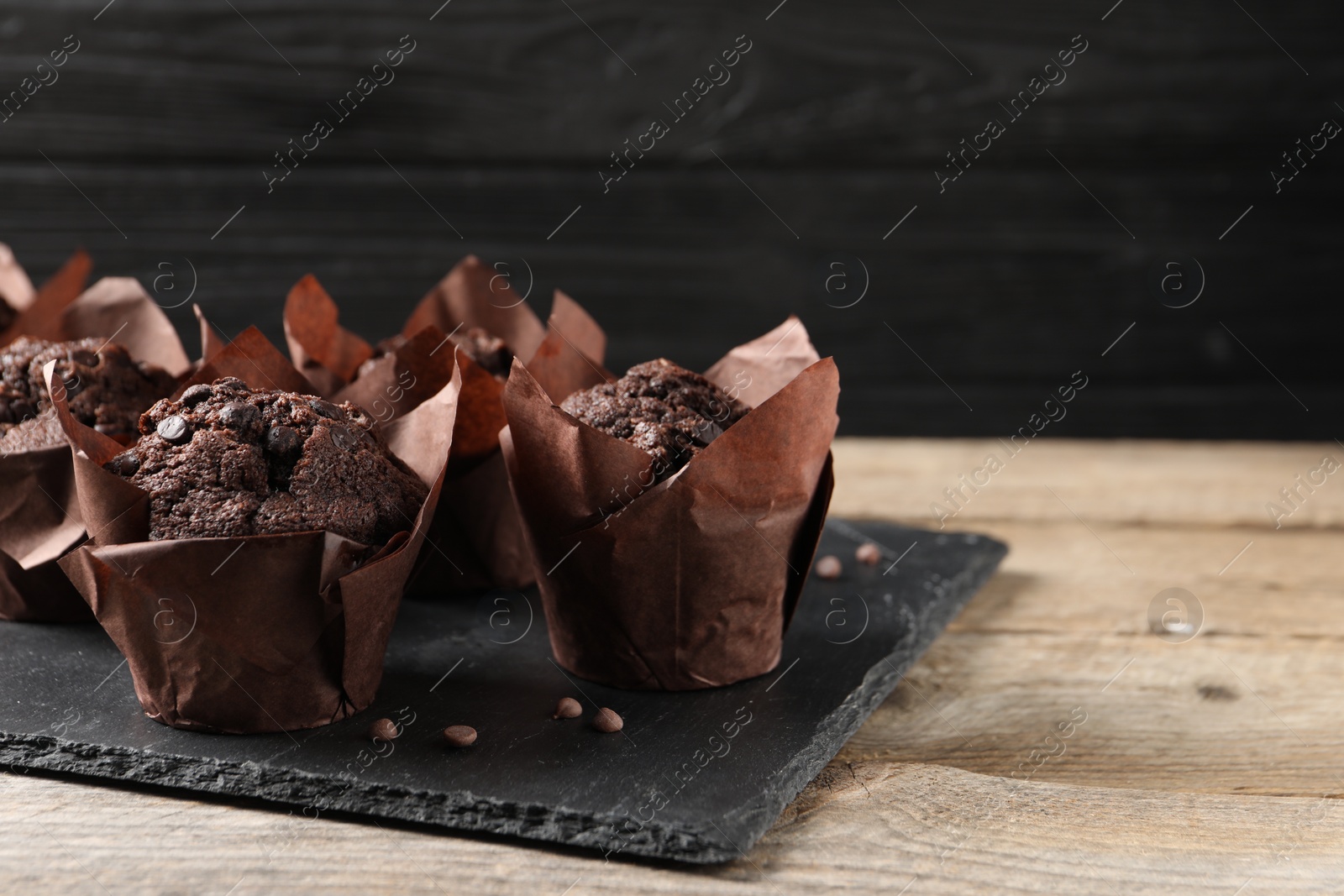 Photo of Delicious chocolate muffins on wooden table. Space for text