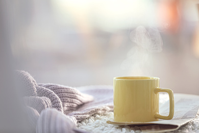 Photo of Cup of coffee, newspaper and knitted sweater near window in morning. Space for text