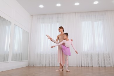 Photo of Little ballerina and her teacher practicing dance moves in studio