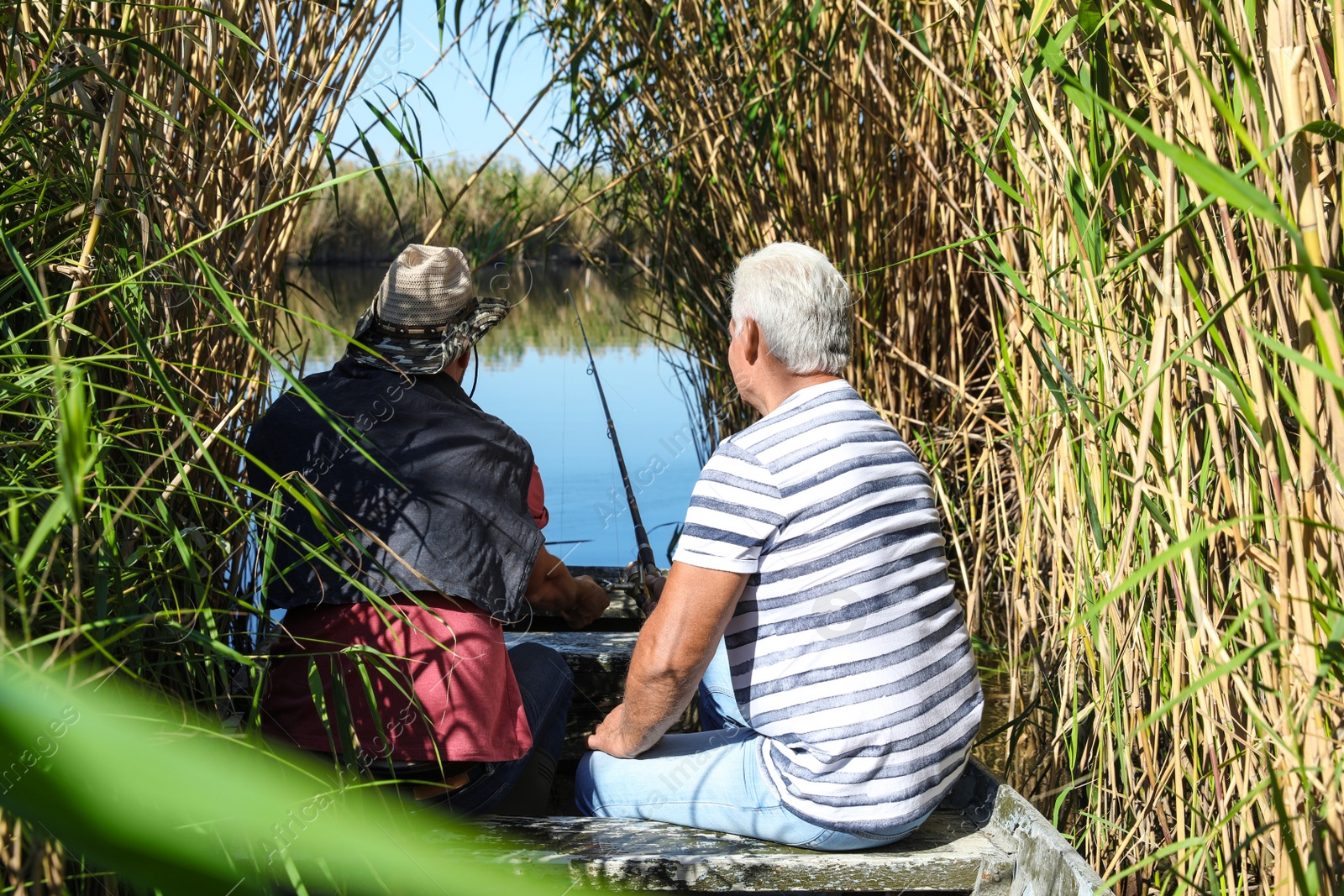 Photo of Father and adult son fishing together from boat on sunny day