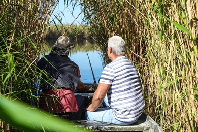 Father and adult son fishing together from boat on sunny day