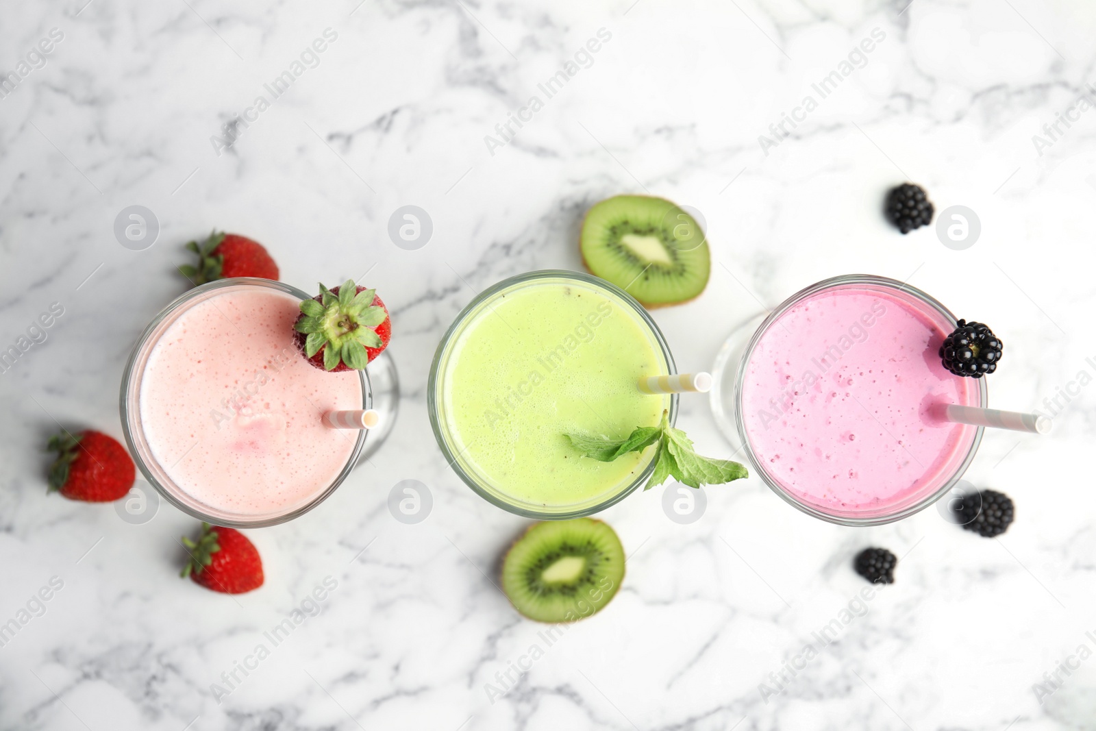 Photo of Tasty milk shakes with fresh berries on white marble table, flat lay